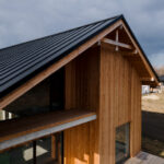 Modern house with a dark metal roof and wooden siding, photographed under a cloudy sky.