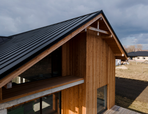 Modern house with a dark metal roof and wooden siding, photographed under a cloudy sky.