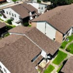 Aerial view of a residential apartment complex with multiple buildings featuring brown shingle roofs and well-maintained green pathways.