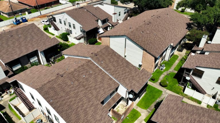 Aerial view of a residential apartment complex with multiple buildings featuring brown shingle roofs and well-maintained green pathways.