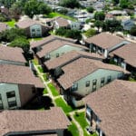 Aerial view of a residential apartment complex featuring multiple brown-shingled buildings, green lawns, and neatly arranged walkways.