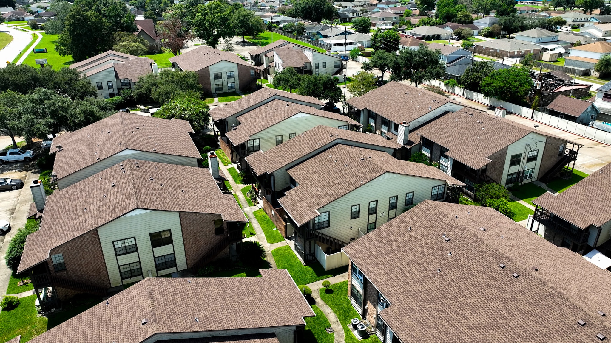 Aerial view of a residential apartment complex featuring multiple brown-shingled buildings, green lawns, and neatly arranged walkways.