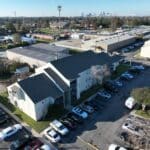 Aerial view of an apartment complex with multiple parked cars along the street and in designated parking areas.
