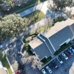 Aerial view of a residential building with a pitched roof and nearby parked cars.