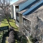 Aerial view of the Towne-Bridge Place Apartments sign and building exterior, featuring balconies, bare trees, and a neatly landscaped walkway.